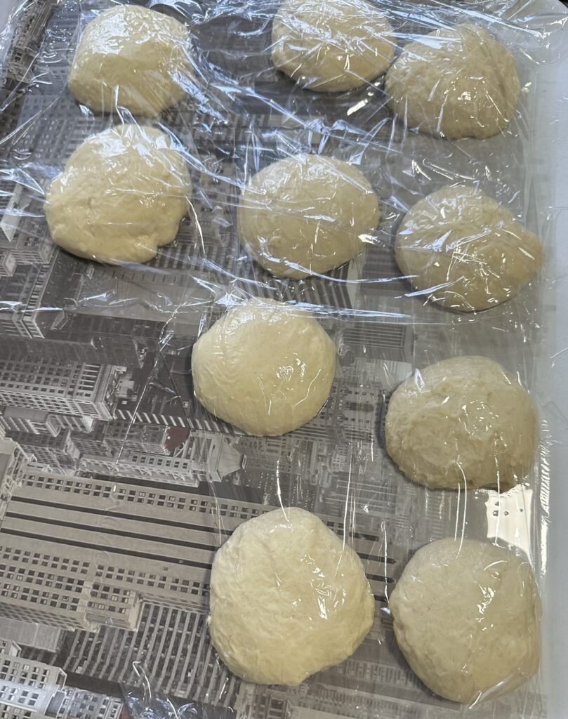 ten balls of dough on a tray covered with transparent film