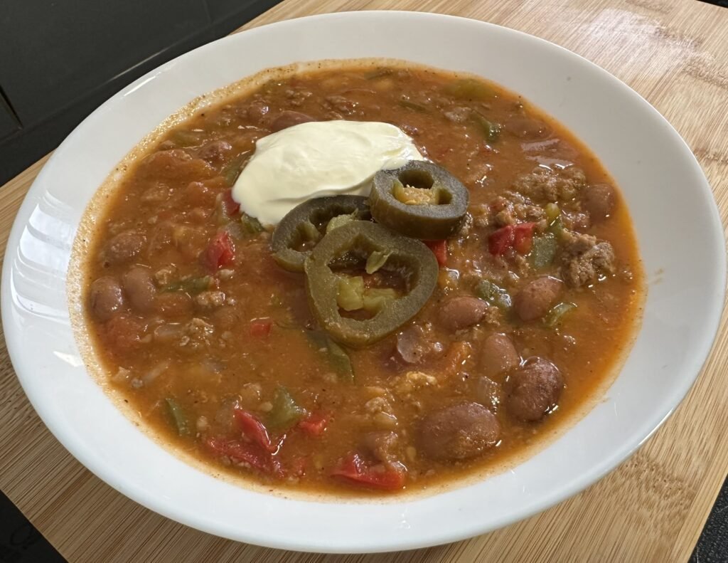 Chili con carne with sour cream and sliced jalapenos