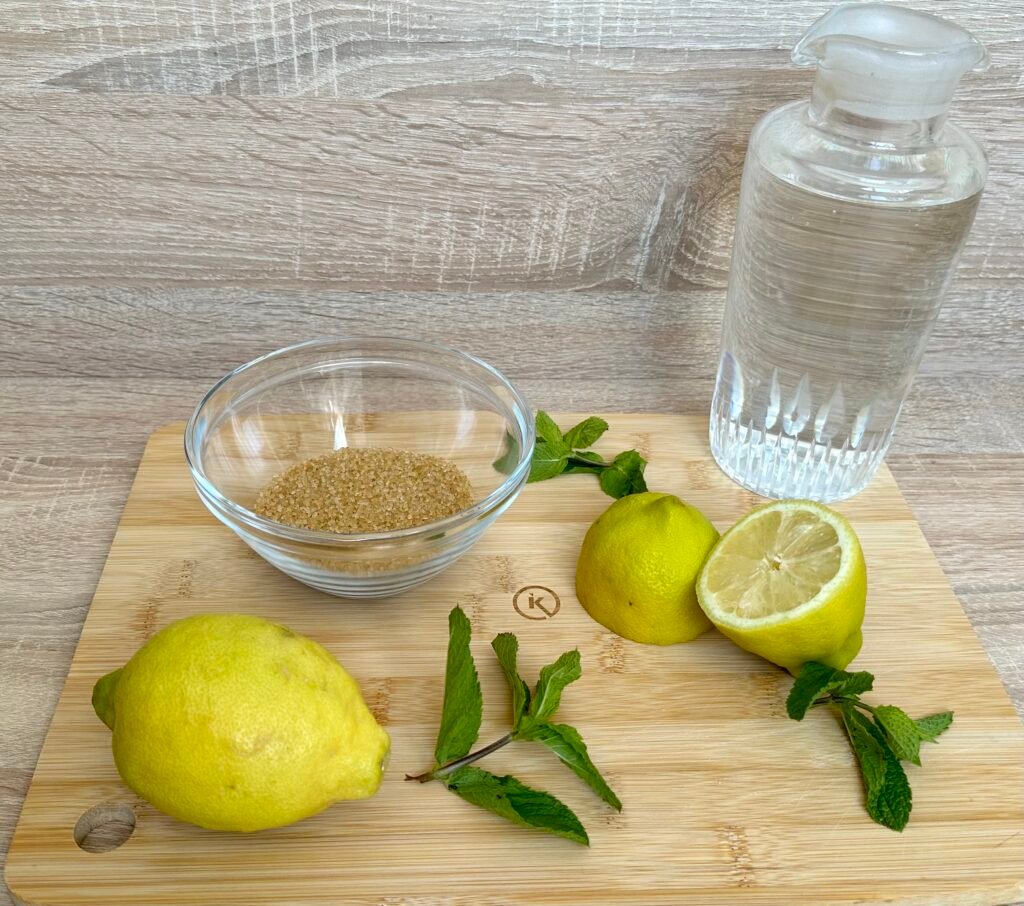 Ingredientes para hacer una refrescante limonada casera. Limones, ramitas de menta, azúcar moreno y agua filtrada.