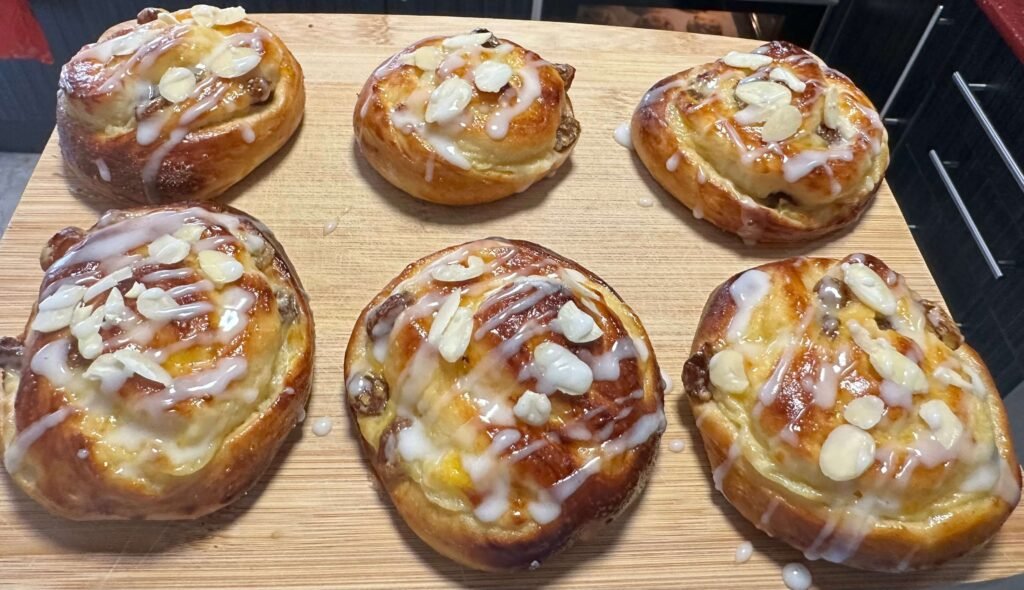 Coffee buns with cream and raisins decorated with icing and rolled almonds on a wooden board
