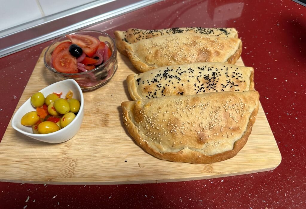 Empanadas on a wooden board with olives and tomato