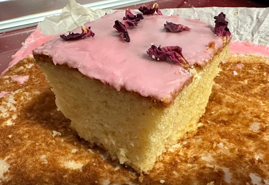 Piece of sponge cake decorated with pink icing and rose petals