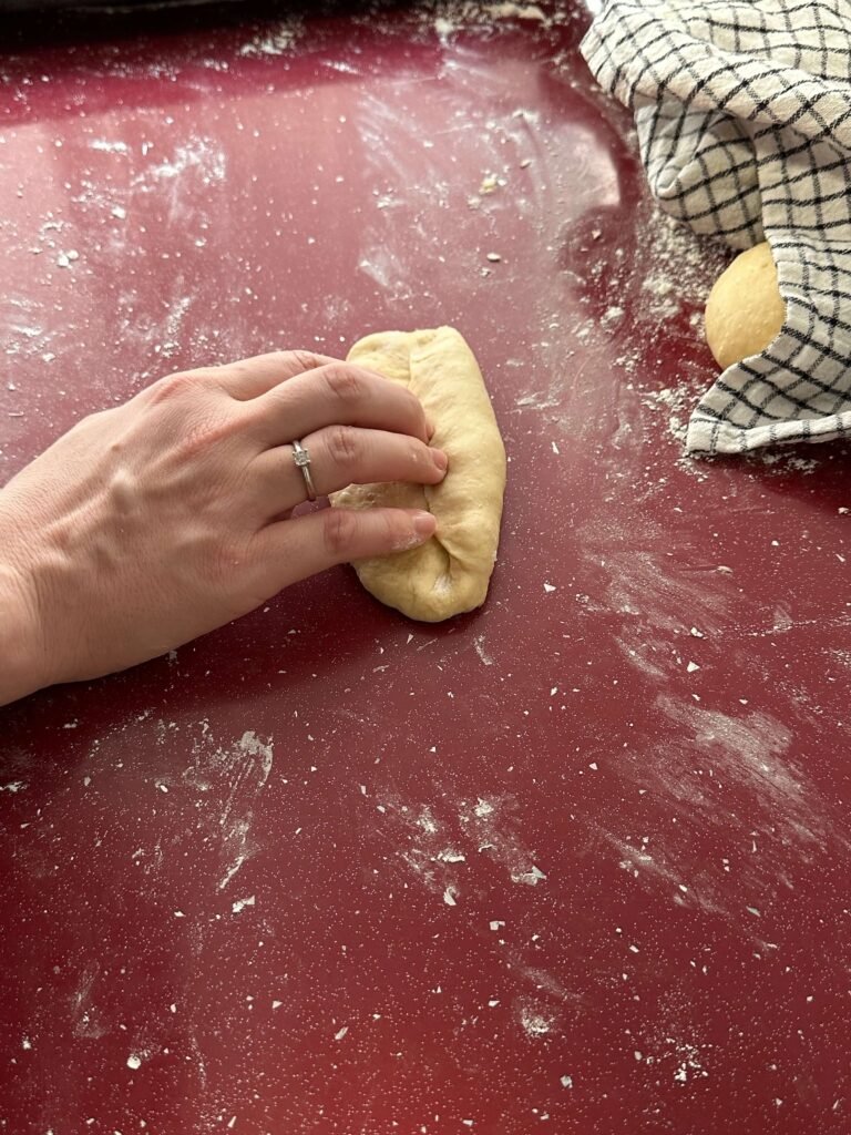 A hand manipulating dough to make hotdog buns