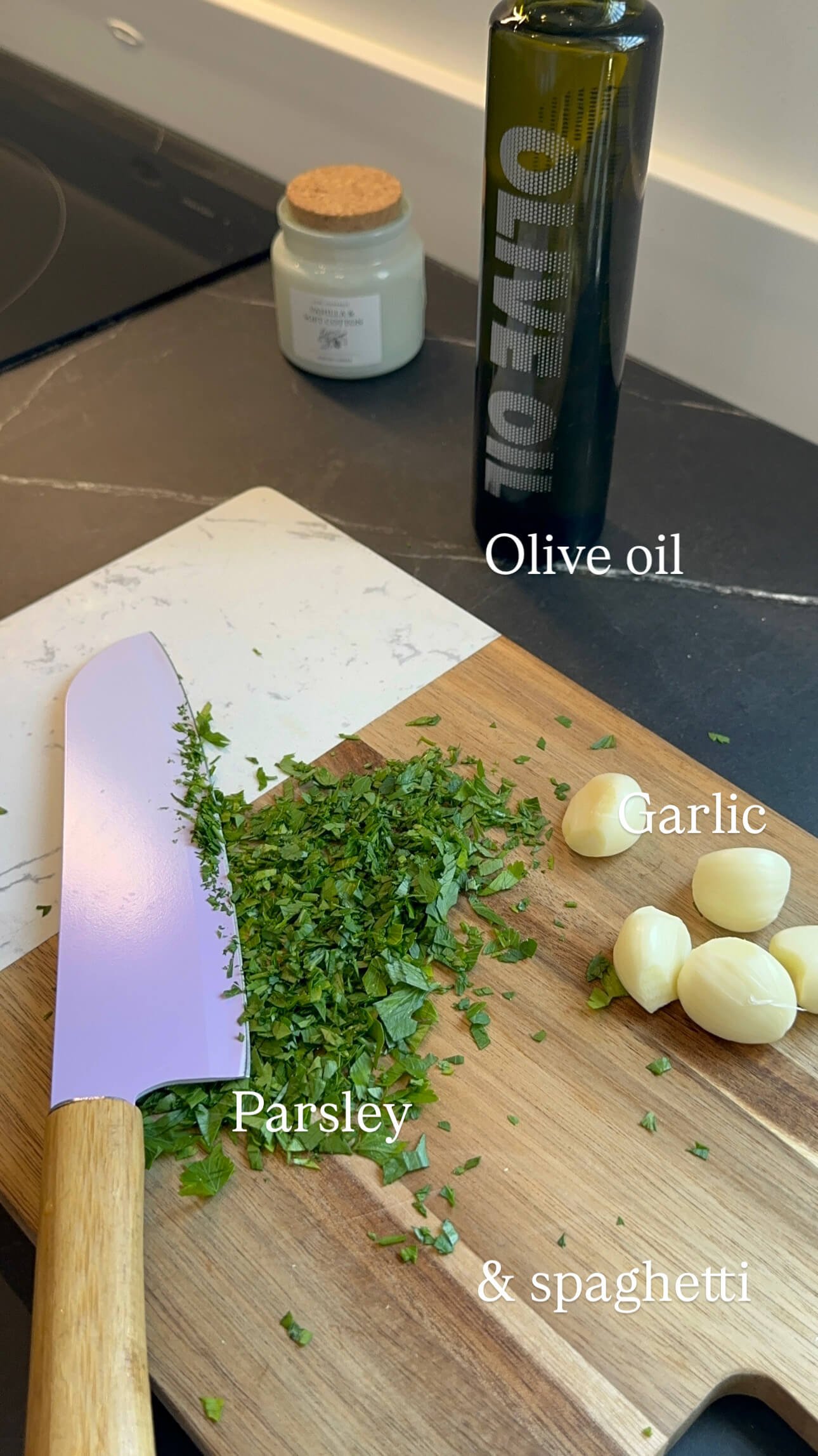 cutting board with garlic cloves, chopped parsley, and a bottle of extra virgin olive oil