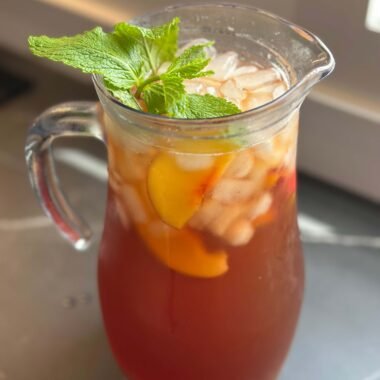 jarra con té helado de nectarina con cubitos de hielo, trozos de nectarina y menta