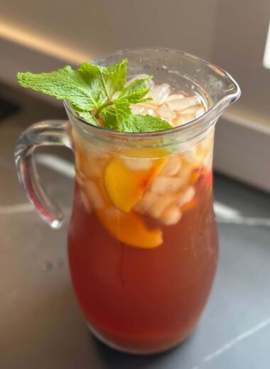 Pitcher of nectarine iced tea with ice cubes, nectarine chunks, and mint