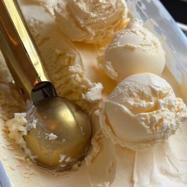 Vanilla ice cream tub with three scoops of ice cream and a golden spoon