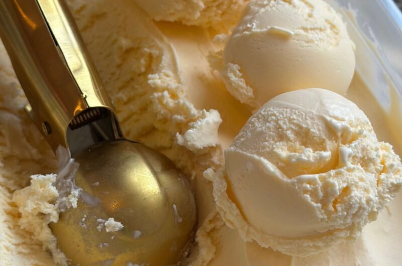 Vanilla ice cream tub with three scoops of ice cream and a golden spoon