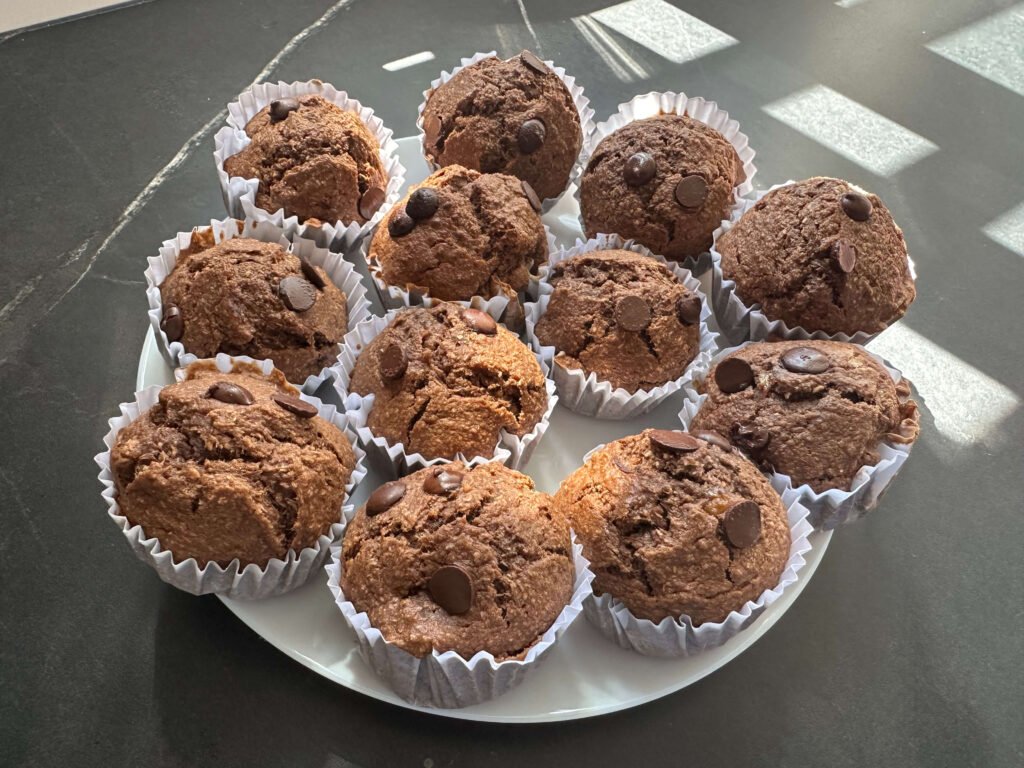 Plato blanco de una encimera negra con varios muffins saludables de coco plátano y chocolate