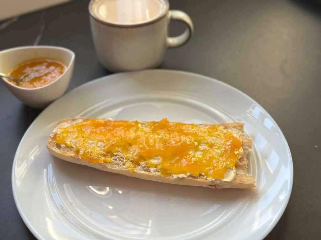 tostada con mantequilla y mermelada de mango, un cuenco con mermelada de mango y una taza de café con leche